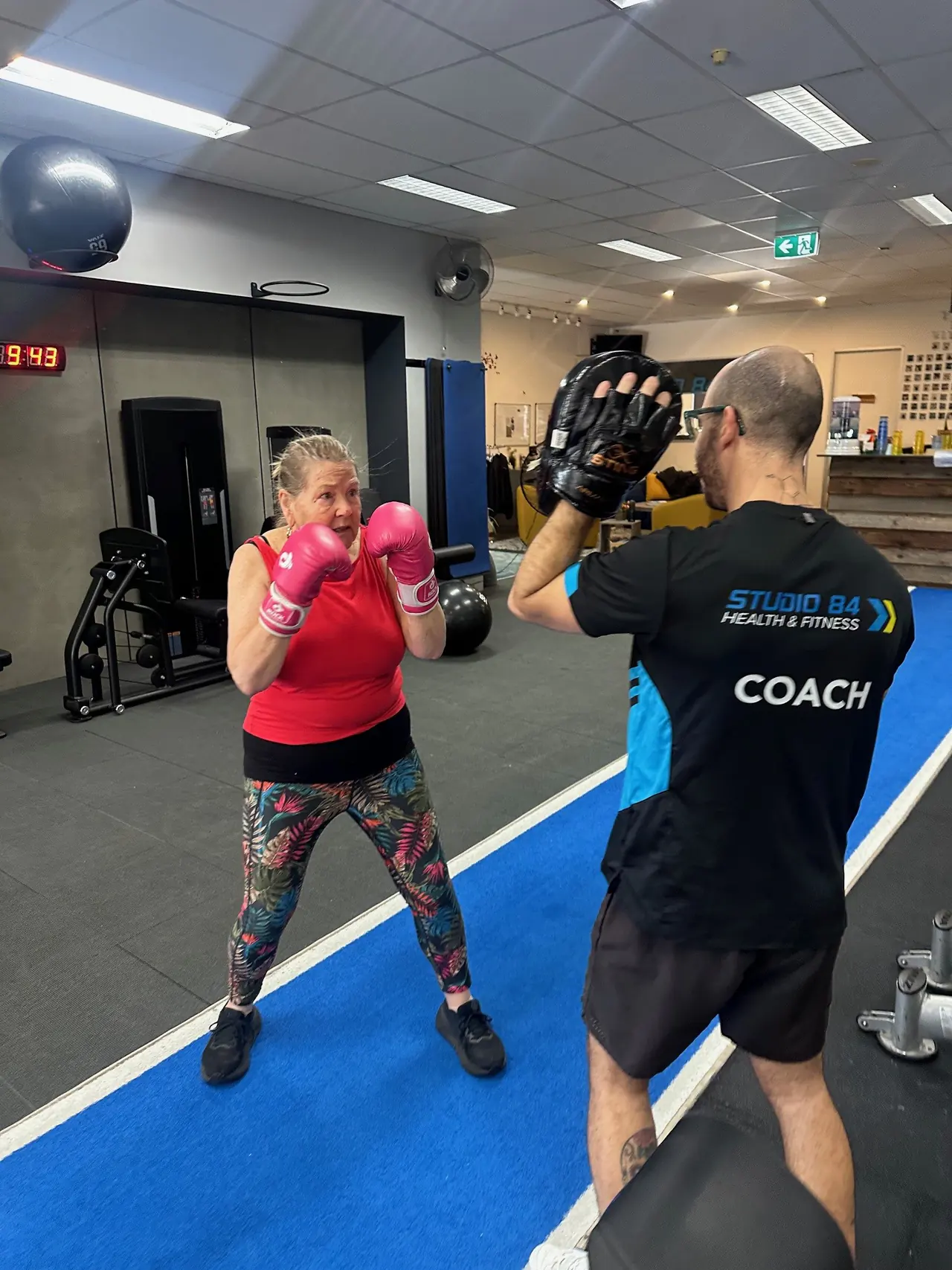 Member Margie, in her 70s, boxing pads with a Studio 84 coach