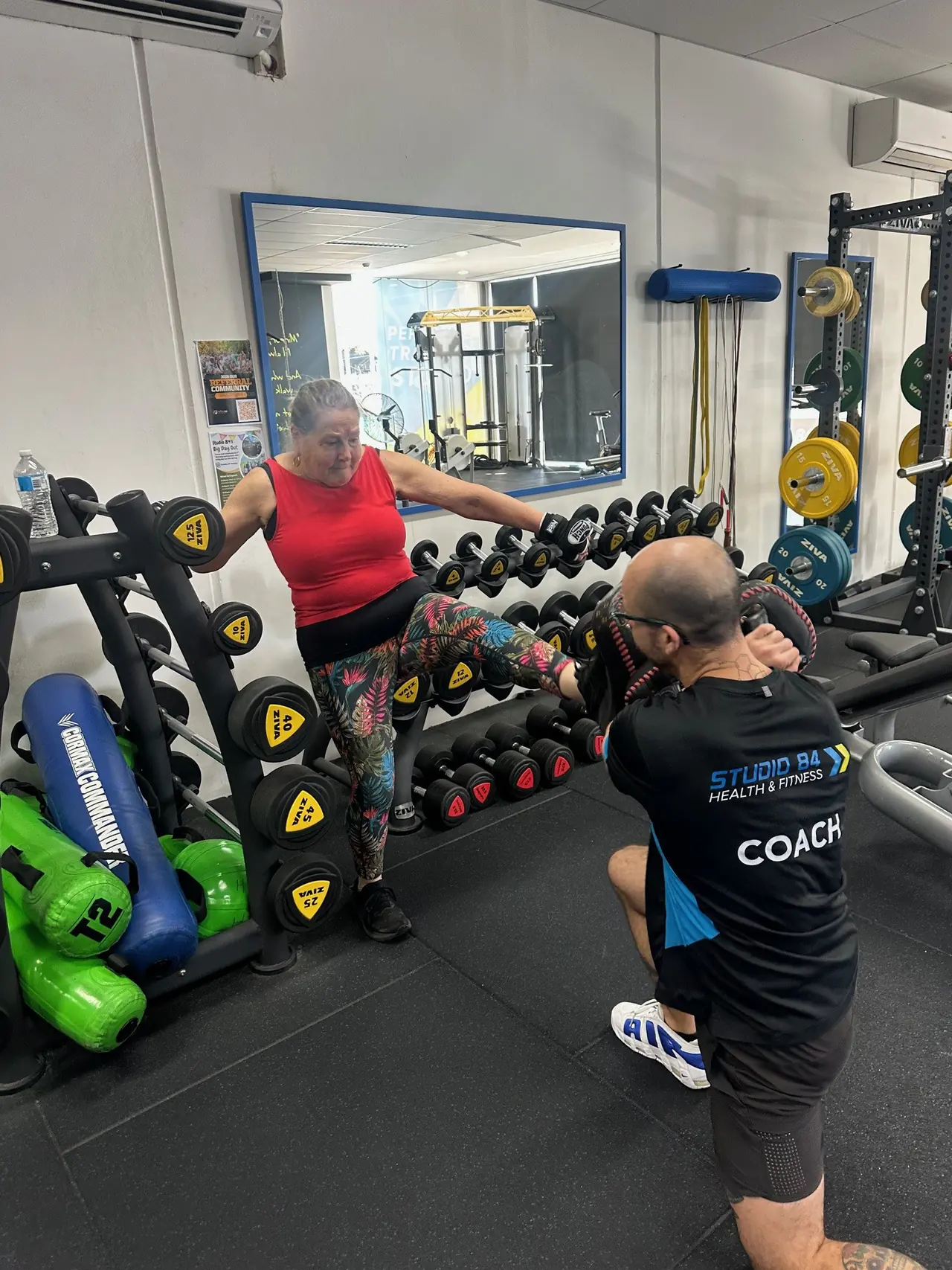 A member training with dumbbells while her coach kneels beside her